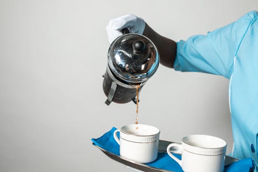 Close-up of a person serving coffee from a French press into cups, showcasing hospitality.