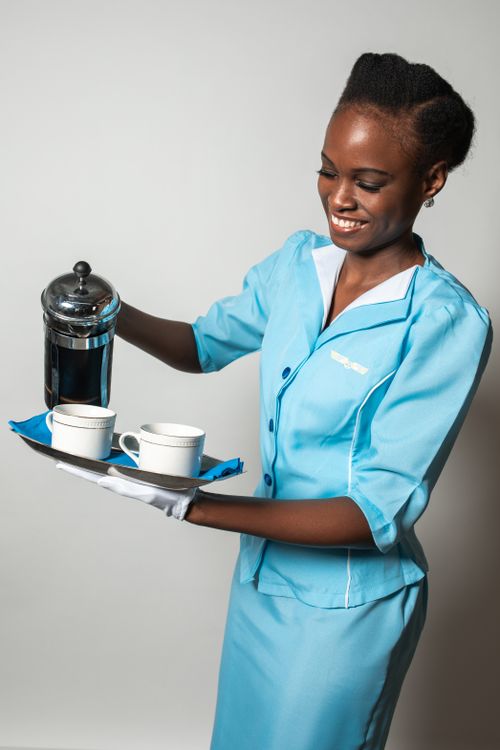 Free Flight attendant in blue uniform serving coffee with a smile, showcasing hospitality. Stock Photo