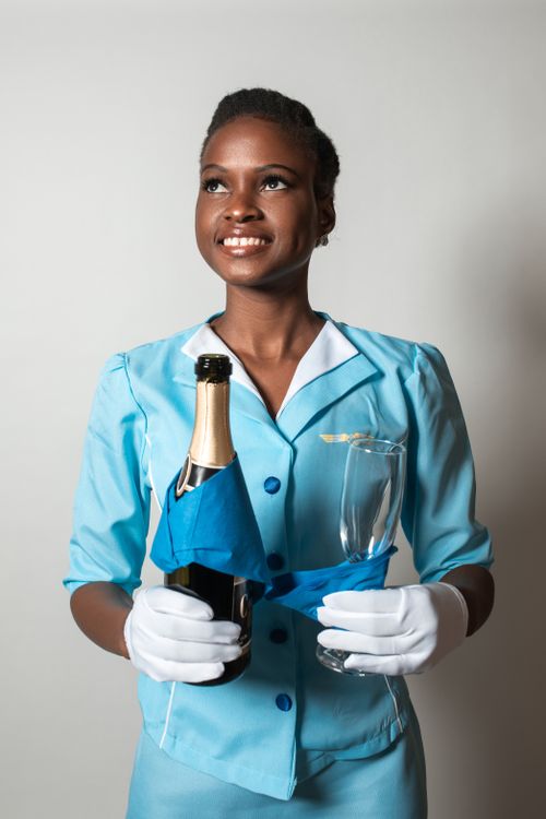 Free Smiling stewardess in a blue uniform holding a champagne bottle and glass with a white background. Stock Photo