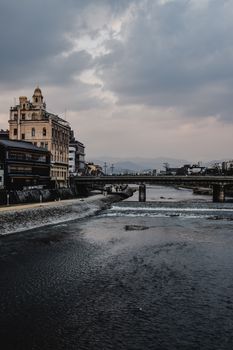 京都河畔的建筑在阴云密布的天空下，与宁静流淌的河水共同构成了一幅富有戏剧性的景色