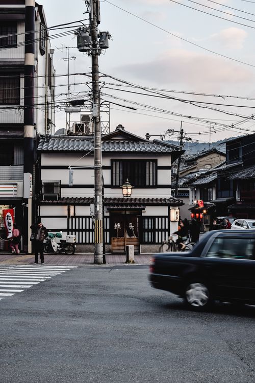 Free A bustling street in Kyoto, Japan at twilight featuring traditional buildings and passing vehicles. Stock Photo