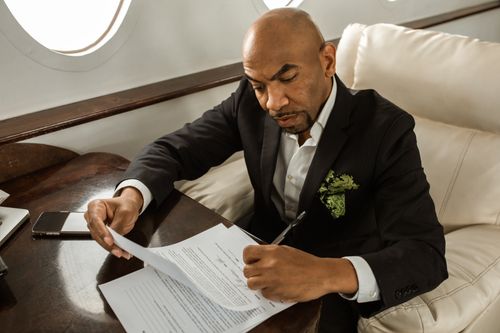 Free Serious businessman in black suit signing papers onboard a private jet, focusing on work. Stock Photo