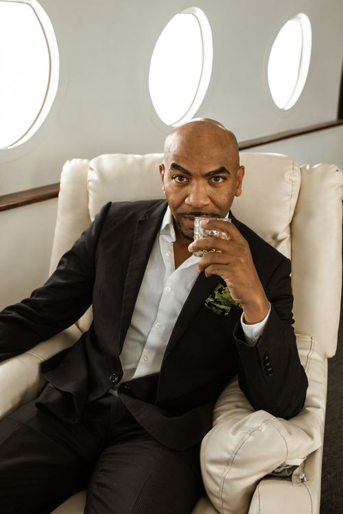 Free Businessman in black suit enjoying a drink while flying in a private jet, illustrating luxury and travel lifestyle. Stock Photo