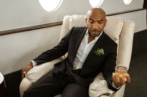 Free Elegant man in suit enjoying whiskey in stylish airplane cabin. Stock Photo