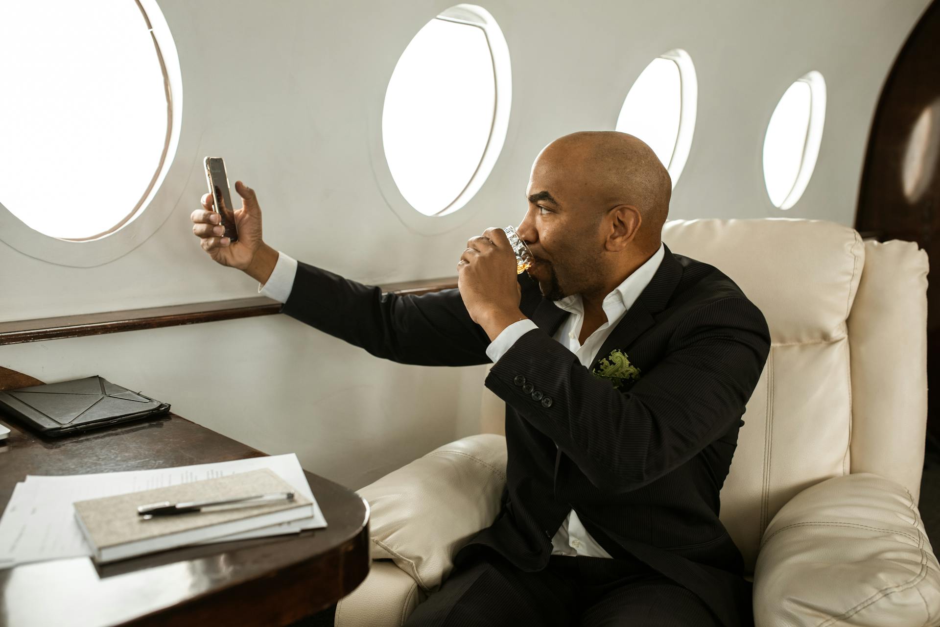 Businessman enjoying a drink while video calling in a private jet. Luxurious travel experience.