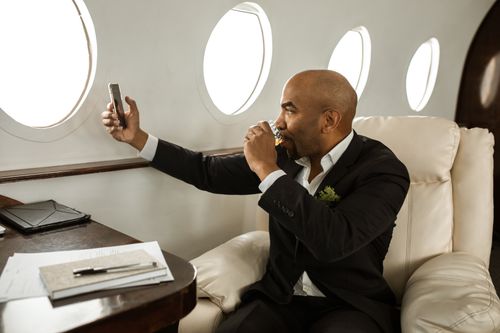 Free Businessman enjoying a drink while video calling in a private jet. Luxurious travel experience. Stock Photo