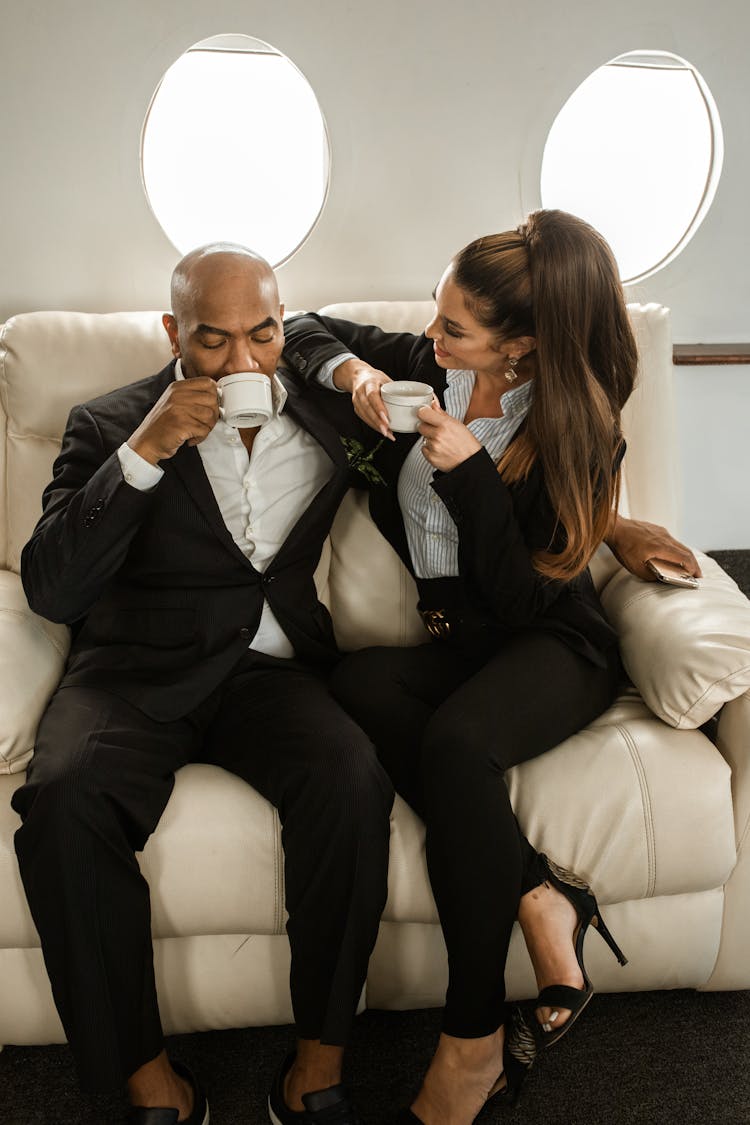 A Man Sipping Coffee Next To A Woman On An Airplane