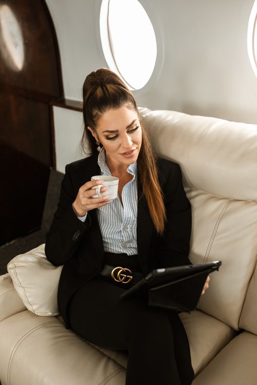 Free Woman in business attire using tablet and drinking coffee on a private jet. Stock Photo
