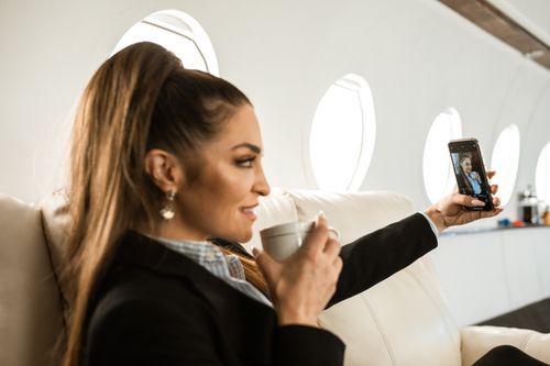 Free A woman comfortably enjoys a coffee while taking a selfie in a luxurious private jet. Stock Photo