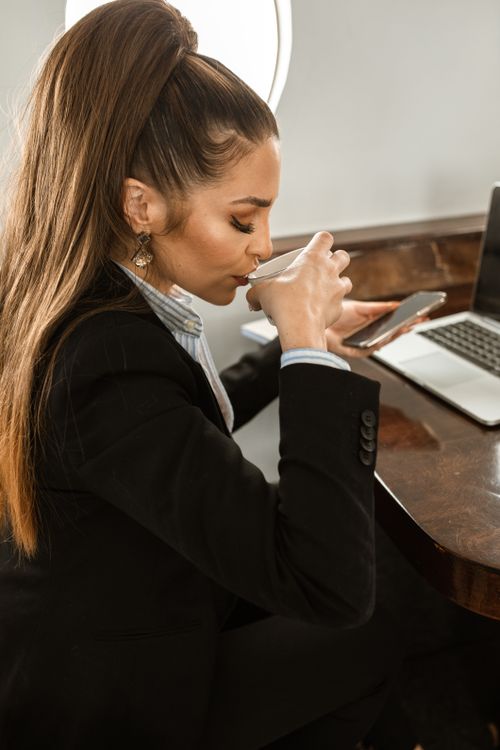 Free Confident businesswoman enjoying coffee in a stylish office setting, holding a smartphone. Stock Photo
