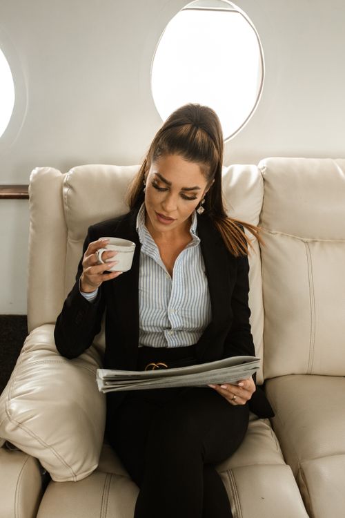Free Confident businesswoman enjoying a coffee and reading on a luxurious flight. Stock Photo