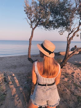Blonde woman in sunhat enjoys tranquil sunset by the sea, embracing leisure and nature.