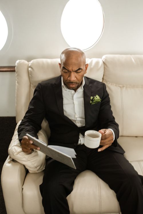 Free Businessman in a black suit reading documents and enjoying coffee on a private jet. Stock Photo