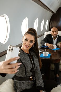 Elegant business professionals enjoying a luxury flight taking a selfie on a private jet.