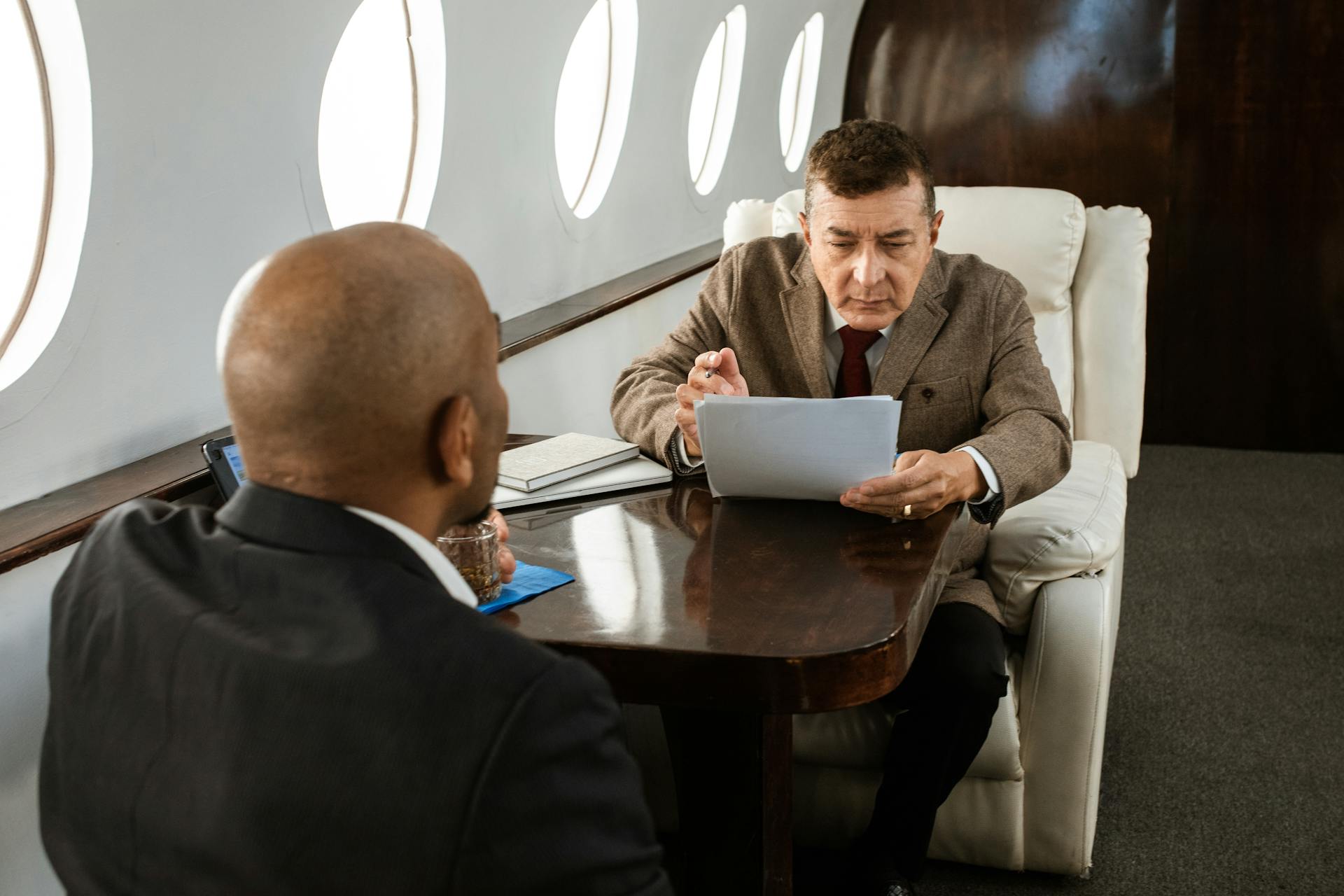 Two businessmen discussing documents in a luxury private jet, focused and professional.