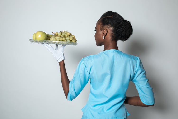 Backview Of A Flight Attendant Carrying Serving Tray Full Of Fruits 