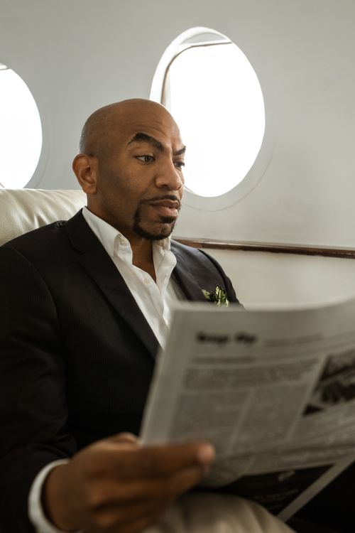 Free African American man in suit reading newspaper in private jet. Focused and relaxed. Stock Photo