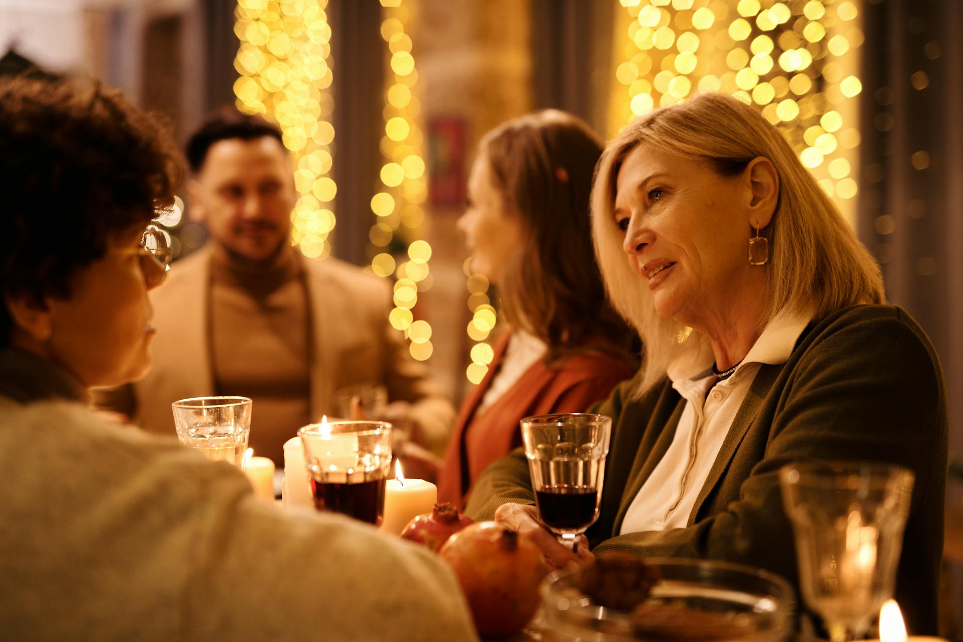 A warm holiday gathering with family and friends enjoying dinner with festive lights.