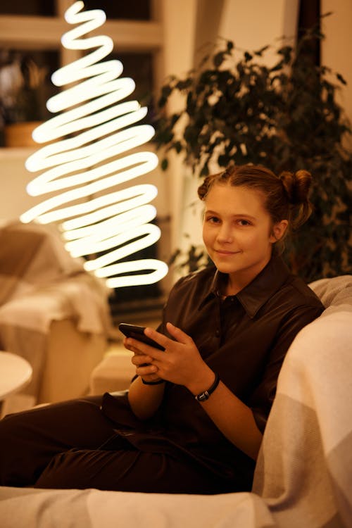 光沢のあるランプの近くのソファでスマートフォンと10代の笑顔