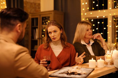 Free Three people enjoying a festive dinner table conversation surrounded by warm holiday lights. Stock Photo