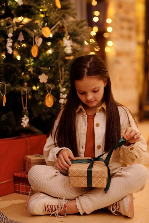 Free A young girl joyfully opens a Christmas present beside a decorated tree. Stock Photo