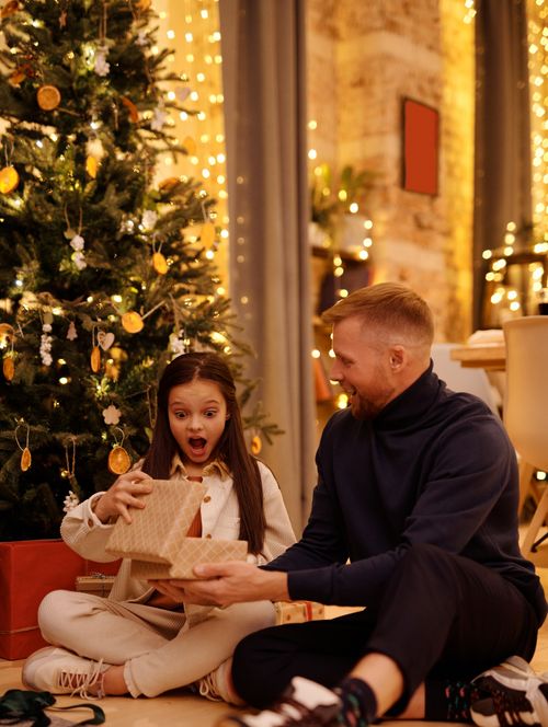 Free Amazed kid with present box between cheerful parent and Christmas tree during New Year holiday at home Stock Photo