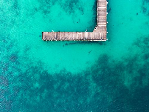 Free Stunning aerial shot of a wooden jetty extending over vibrant turquoise waters. Ideal for travel destinations. Stock Photo