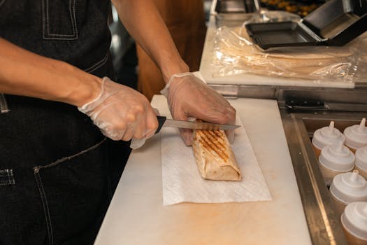 A close-up of a person's hands slicing a shawarma on a kitchen counter, showcasing food preparation.