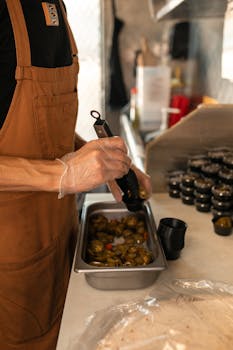 Chef wearing an apron prepares jalapeno peppers in a commercial kitchen setup.