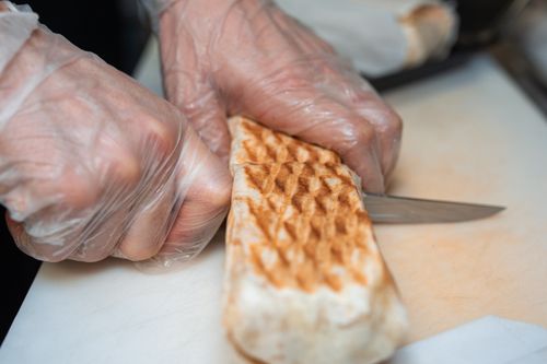 Free Close-up of hands slicing shawarma with a knife on a cutting board. Stock Photo
