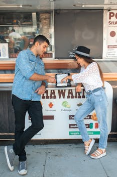 A couple leaning against a shawarma food truck, enjoying a casual meal outdoors.