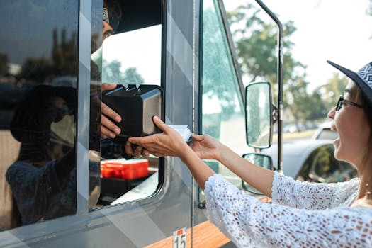 A joyful woman receives a boxed meal from a food truck window on a sunny day.
