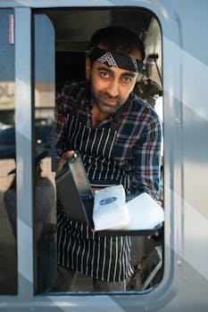 Smiling food truck vendor serving delicious shawarma through a window.
