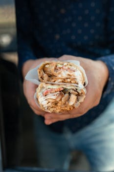 Delicious fresh shawarma wrap held in hands, showing vibrant ingredients and textures.
