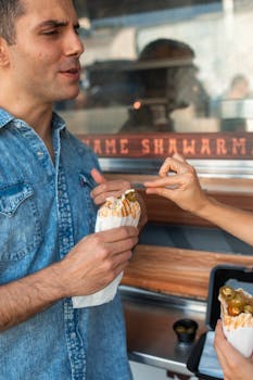 A man enjoying shawarma outdoors at a food truck, engaging in casual conversation.