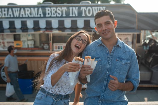 Two friends laughing and eating shawarma from a food truck labeled 'Shawarma Best in Town'.