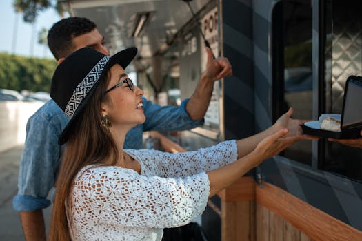 Two friends enjoying outdoor dining at a food truck on a sunny day.