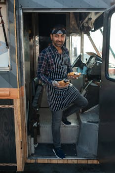 Smiling vendor in a food truck serving delicious street food to customers.