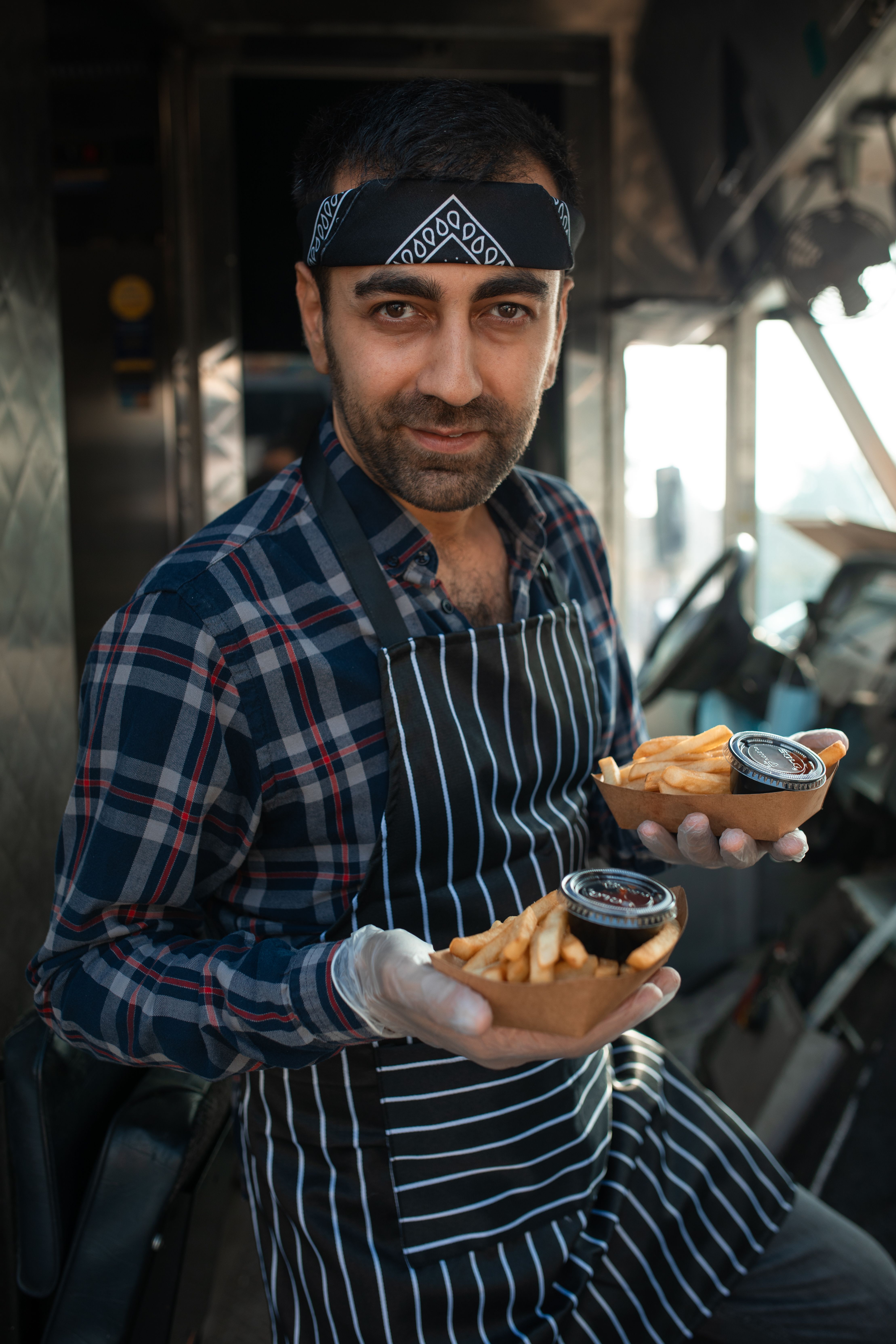 Vendeur en tablier tendant deux barquettes de frites avec leur pot de sauce