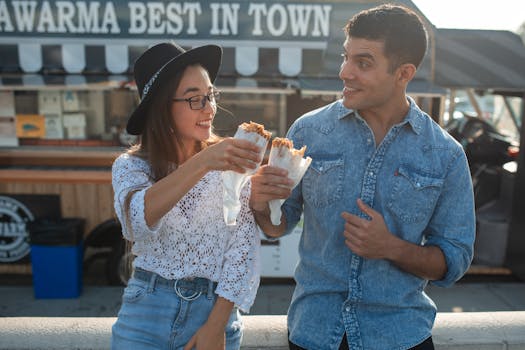Two friends happily eating shawarma in front of a food truck, enjoying leisure time.