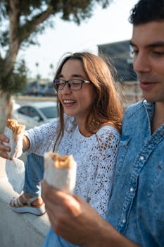 Young friends savoring shawarma outdoors, capturing joyful moments on a sunny day.