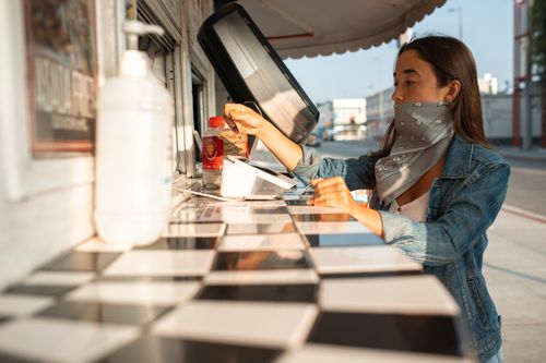 Free A woman in a denim jacket orders food from a street food truck on a sunny day. Stock Photo