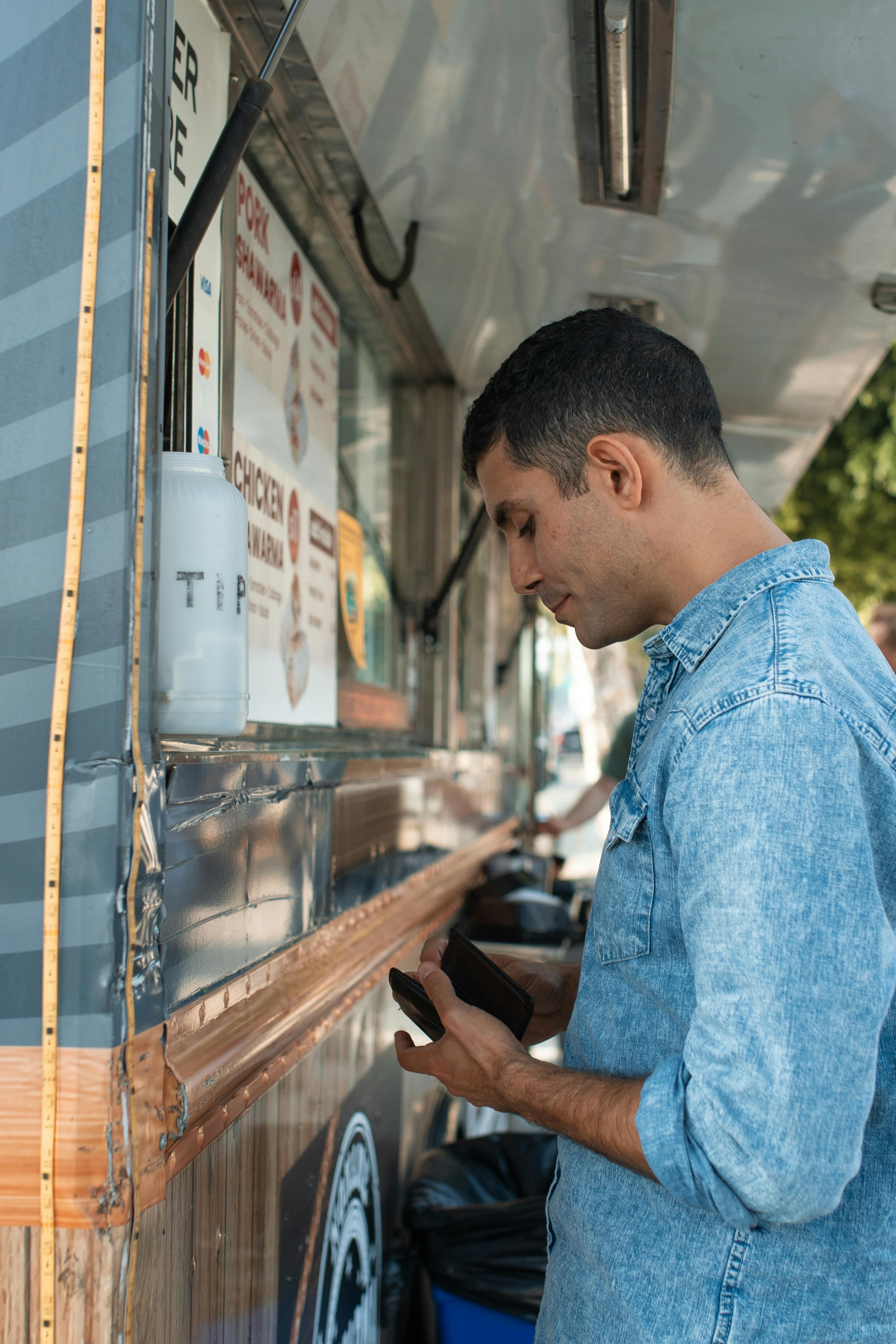 man looking at his wallet while standing beside a food truck