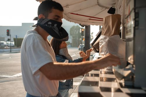 Free Two friends wearing face masks order food at an outdoor stall during the day. Stock Photo
