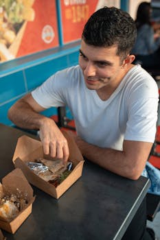 Man eating fast food at a casual indoor setting, smiling and relaxed.