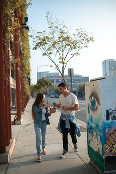 一对年轻夫妇在阳光明媚的城市街道上漫步聊天，周围点缀着街头艺术