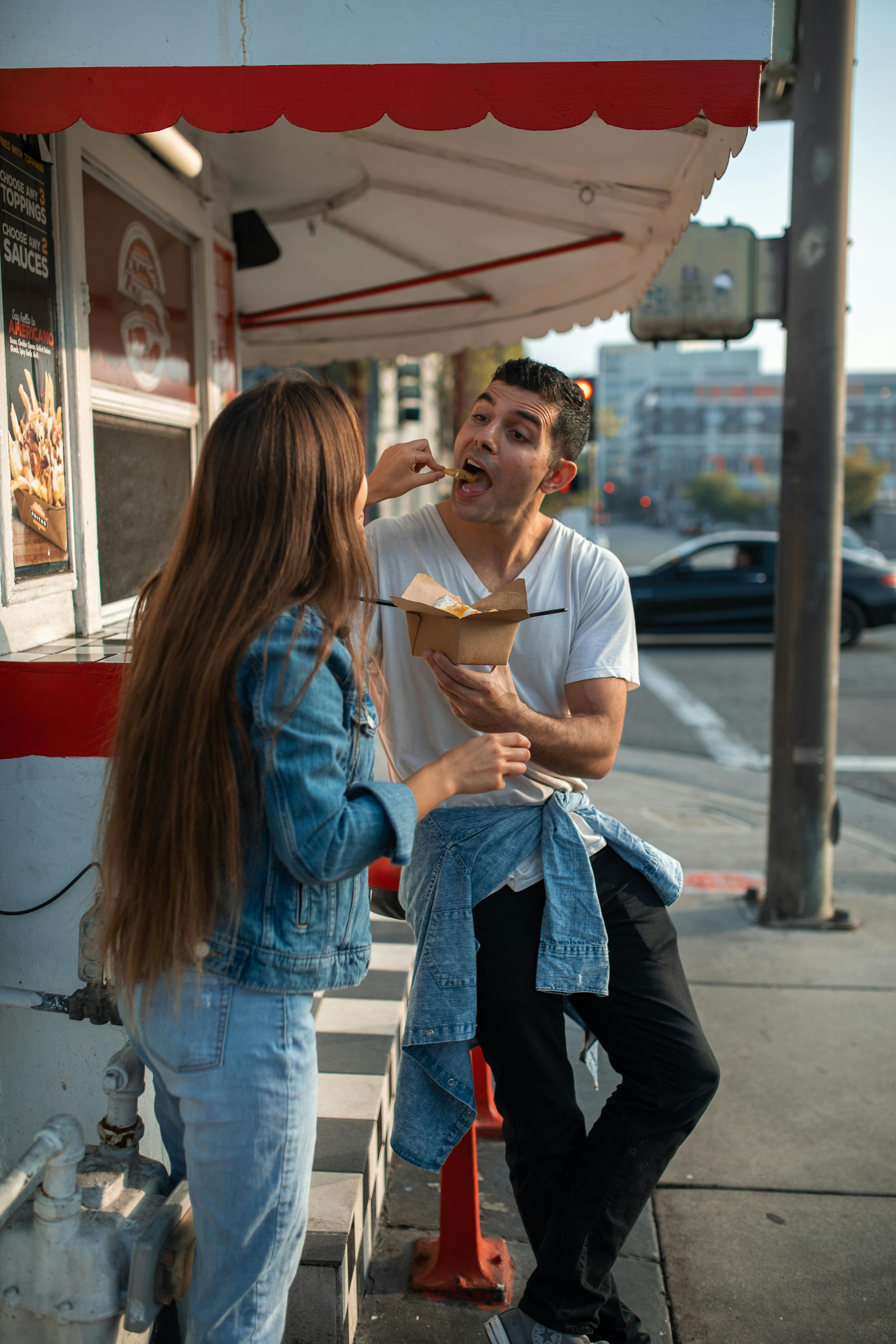 a woman feeding a man in white shirt holding a takeout box