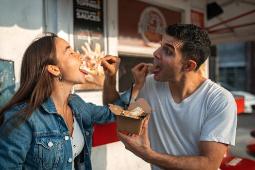 A couple having fun and sharing takeout food while enjoying a sunny day outdoors.
