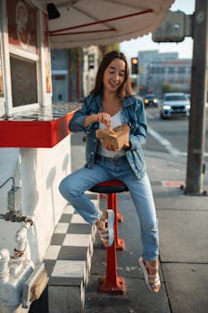 Smiling woman in denim outfit enjoys takeout at street food stand.