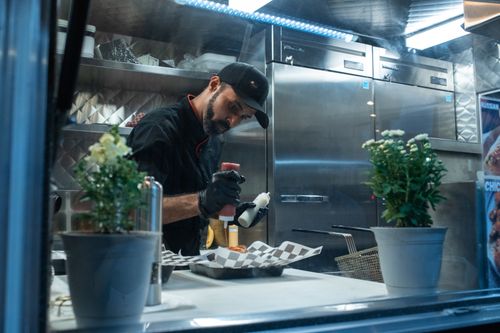 Free A chef skillfully prepares a meal inside a food truck kitchen, showcasing culinary expertise. Stock Photo